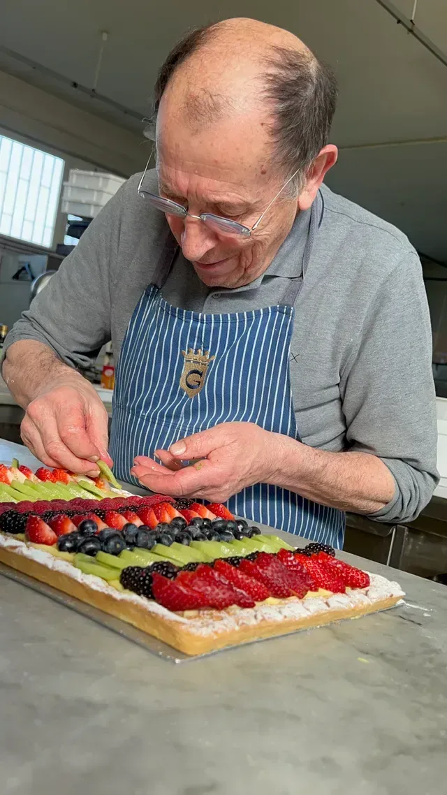 Un uomo con un grembiule sta decorando una torta con la frutta